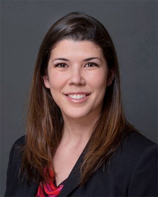 Headshot image of professor, genetic counselor and program contact, Maria Gyure, smiling in front of a gray background. 