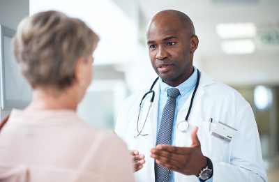 Career-driven, Genetic Counselor employee in lab coat treating a patient by discussing genetic health concerns within a healthcare facility. 